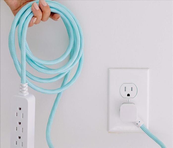 hand holding up extension chord that is plugged into wall