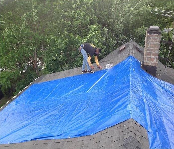  Worker putting blue tarp over damaged roof